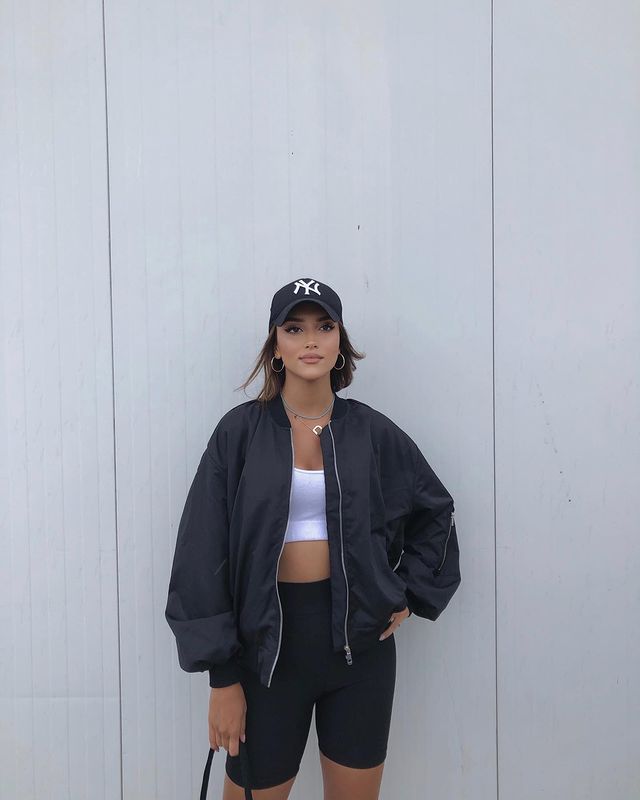 Girl in black Bike shorts, white sports bra and black bomber jacket 