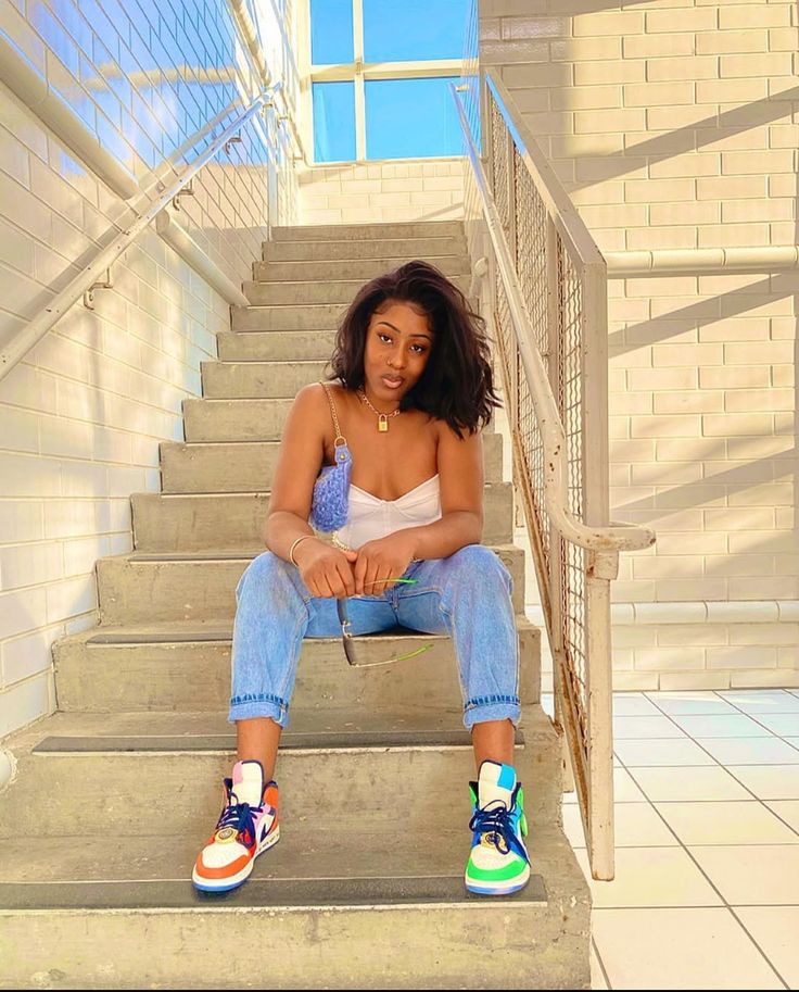 Girl in white strapless top and rolled up blue jeans sitting on the stairs wearing color-pop sneakers