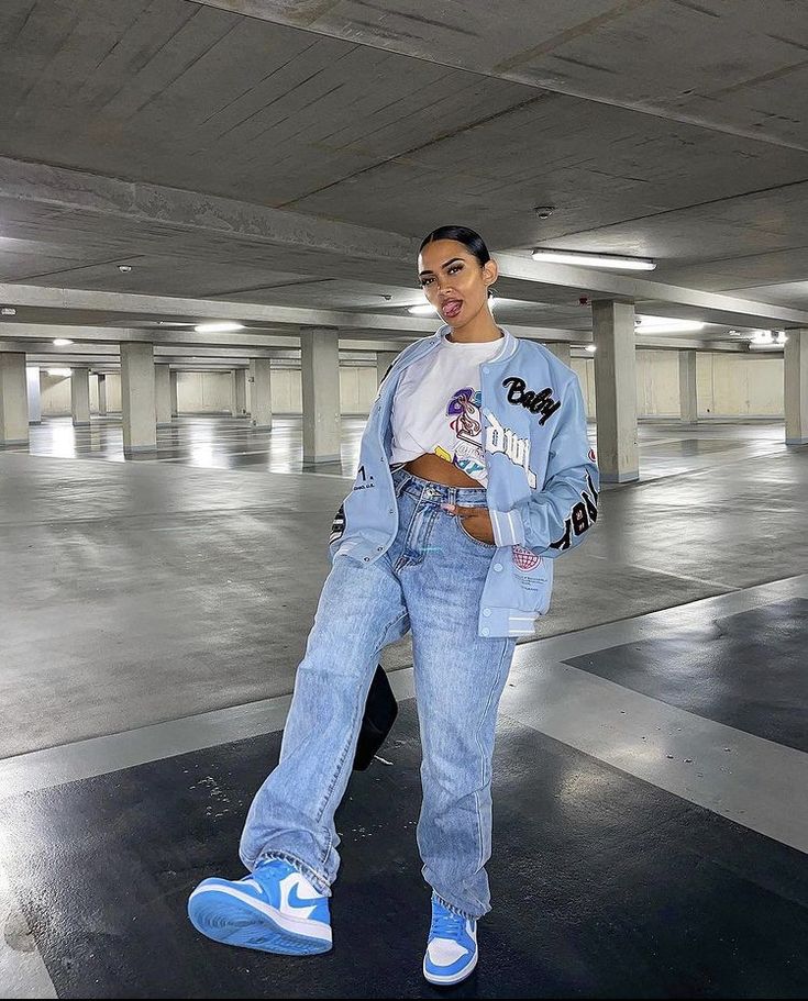 Girl in parking garage wearing school type jacket, croptop, blue jeans, and color-pop sneakers