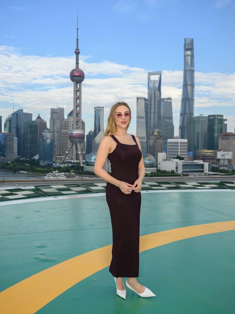 Scarlett Johansson arrived at the “Jurassic World Rebirth” Shanghai photocall wearing a Khaite knitted Dixi midi dress, Prada leather pumps, and Cubitts x Jonathan Bailey Loomis sunglasses.