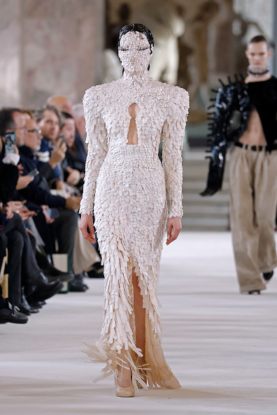 A model goes down the runway for the Schiaparelli Haute Couture Spring/Summer 2024 show, dressed in a long white keyhole neckline embroidered gown that Dua Lipa previously wore to the brand’s Haute Couture Fall/Winter 2025/2026 show