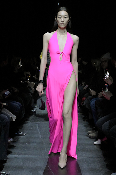 A model walks down the runway at the Balenciaga Fall 2025 fashion show, wearing a neon pink halter neck cutout dress with a knotted bow and hip slit decorations, which Kim Kardashian also wore to the Paris Balenciaga Haute Couture Fall/Winter 2025/2026.