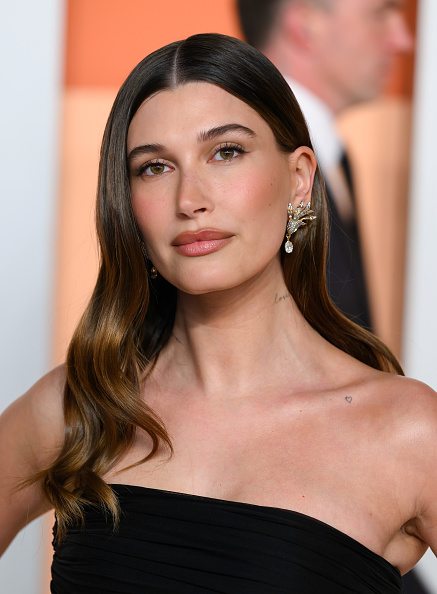Hailey Bieber attended the 2025 Vanity Fair Oscar Party dressed in Tiffany & Co. platinum and 18K gold earrings and a black ruched gown inspired by Yves Saint Laurent’s legendary Spring/Summer 1987 collection.