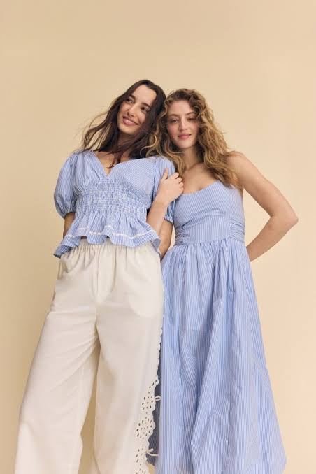 two girls in blue, one in a dress the other in pants with blue top 