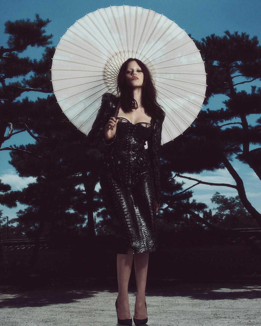 Jenna Ortega is seen cradling a white parasol during the “Wednesday” Season 2 Seoul press tour while dressed in a black lace-up leather midi dress by Dilara Findikoglu.