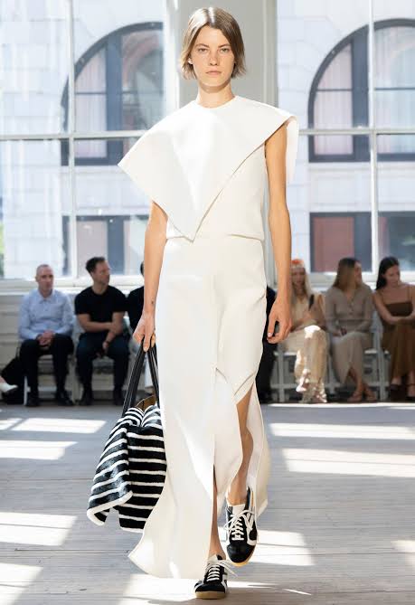 Runway model wearing white dress with poncho type top 