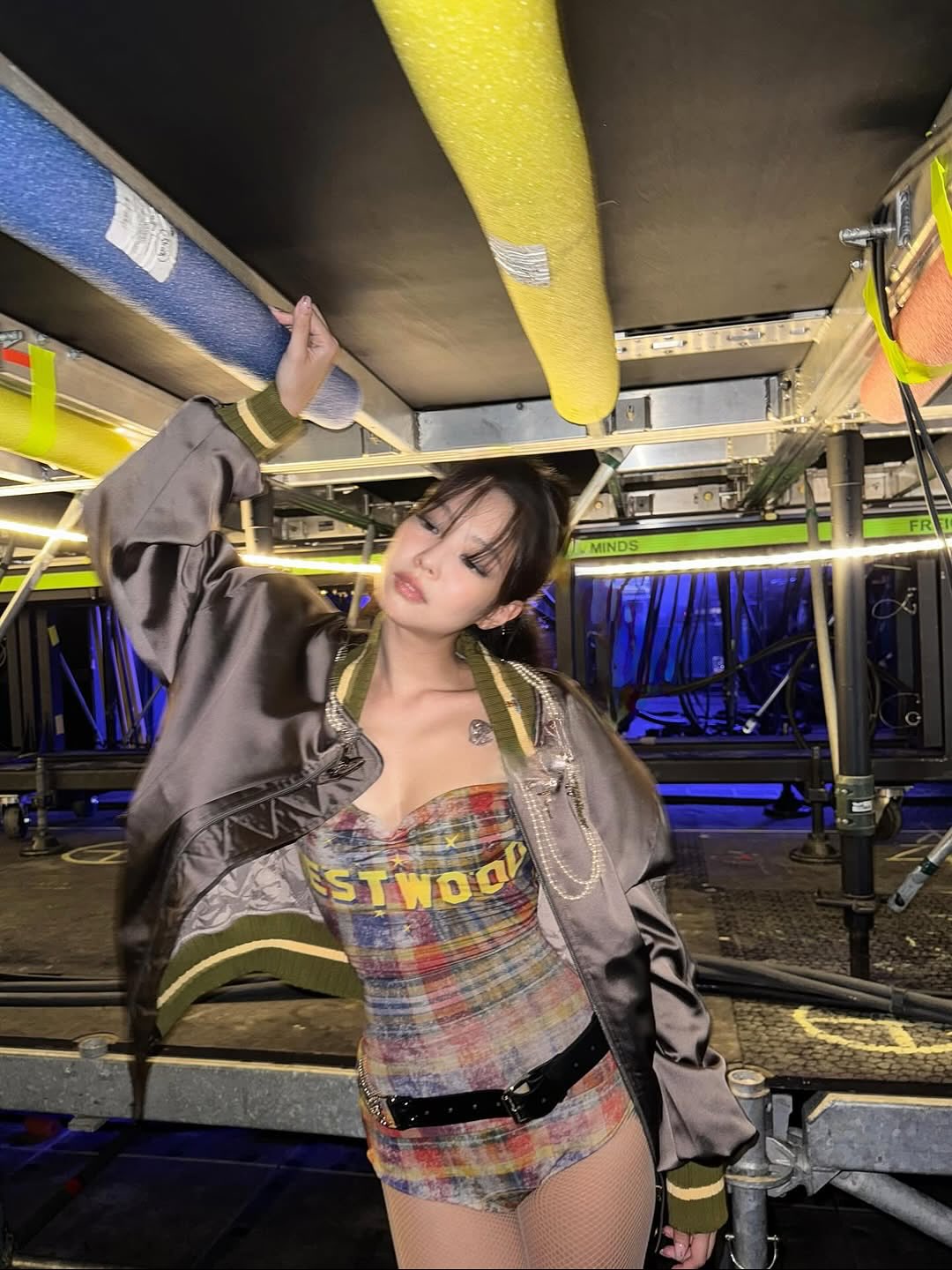 Blackpink Jennie Kim poses backstage at Wembley Stadium during the Deadline World Tour stop in London, wearing a Vivienne Westwood bomber jacket and an Anna top with a tartan pattern and “WESTWOOD” in large yellow block letters, inspired by the iconic HOLLYWOOD sign.