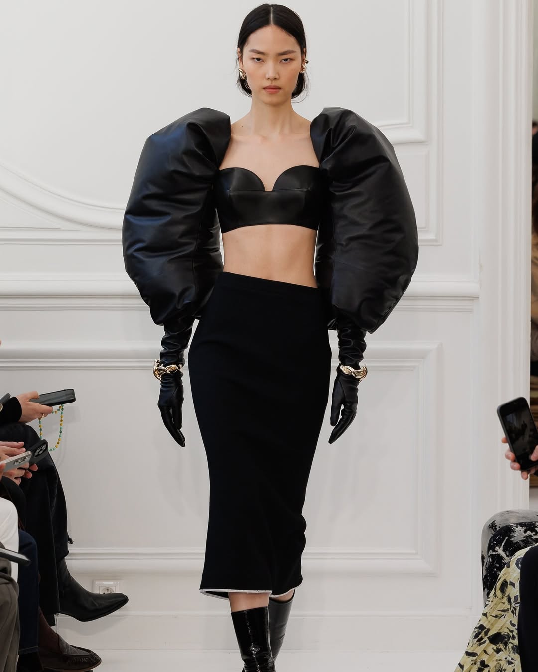 Model Jiahui Zhang shows puff gloves, a bullet bra top, and a mid-length “Kick Back” skirt in cady for Givenchy Womenswear’s Fall/Winter 2025/2026 collection.
