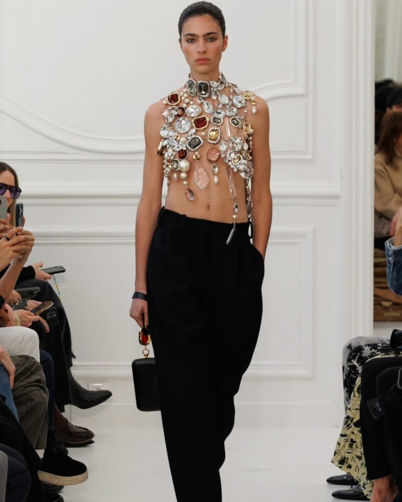 Model Loli Bahia goes down the runway wearing a shattered chandelier jewelry top designed by Sarah Burton for the Givenchy Fall/Winter 2025/2026 collection.