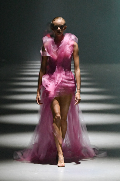 A fashion model is photographed walking the Lever Couture “Velocity of Emotion” ready-to-wear runway collection fashion show in a pink tulle mesh gown.
