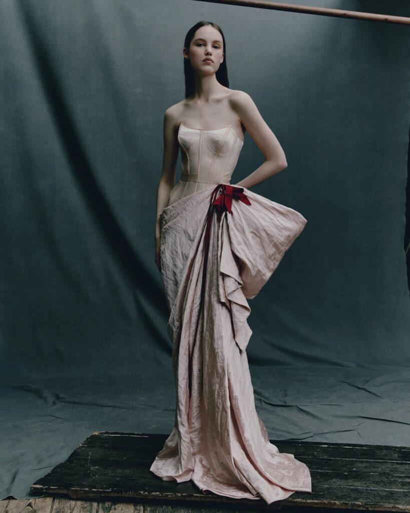 Esther Finch models a strapless corset gown and an asymmetric hand-draped skirt in cameo pink textured satin with red tulip appliques during the Erdem Pre-Spring/Summer 2026 collection fashion show.
