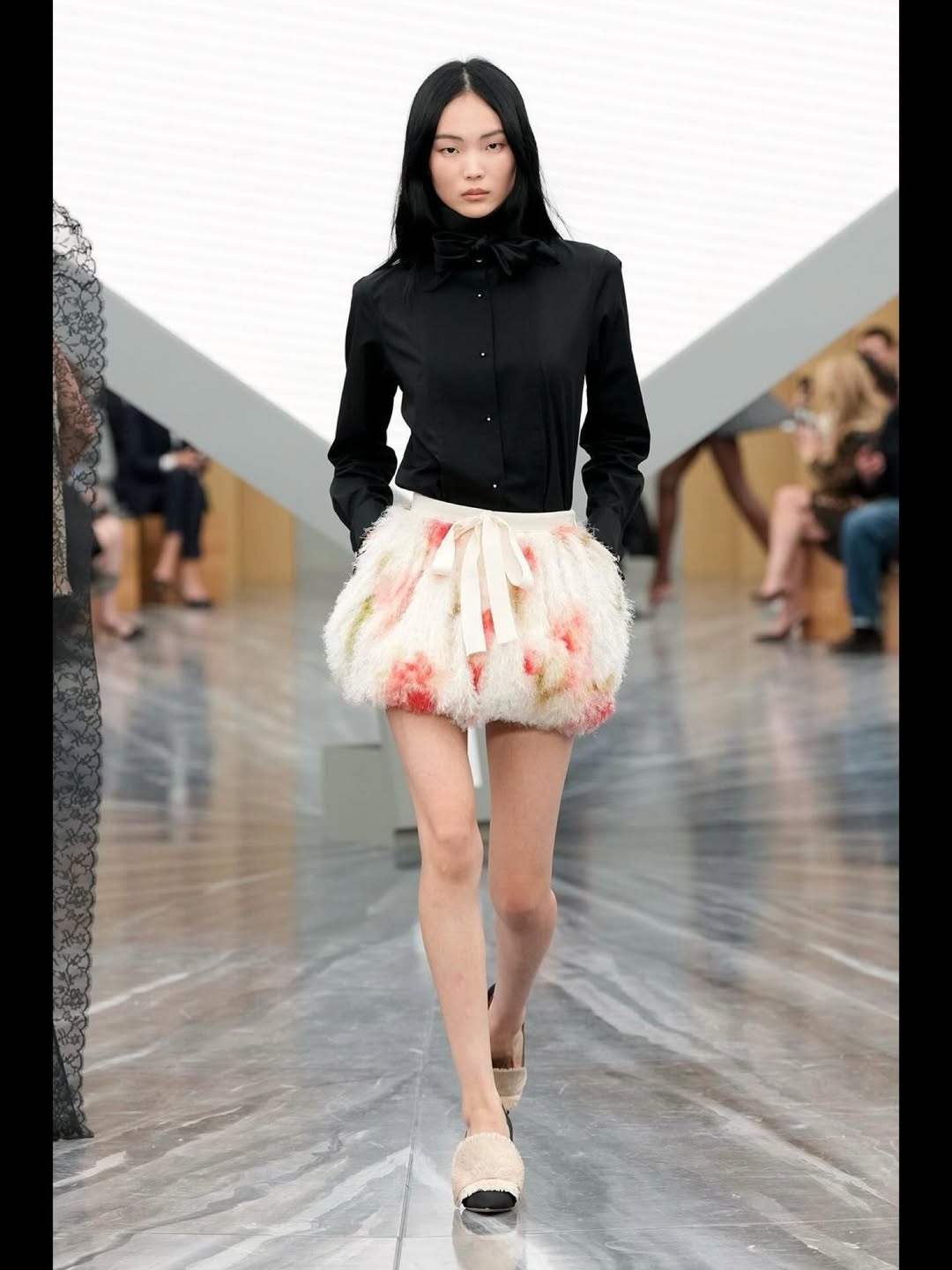 Yun-seo Woo, a fashion model, walks the runway at the Christian Dior Womenswear Spring/Summer 2026 ready-to-wear collection show, wearing a black long-sleeved shirt with a matching bow tie and an embroidered bow-tie bubble short skirt.