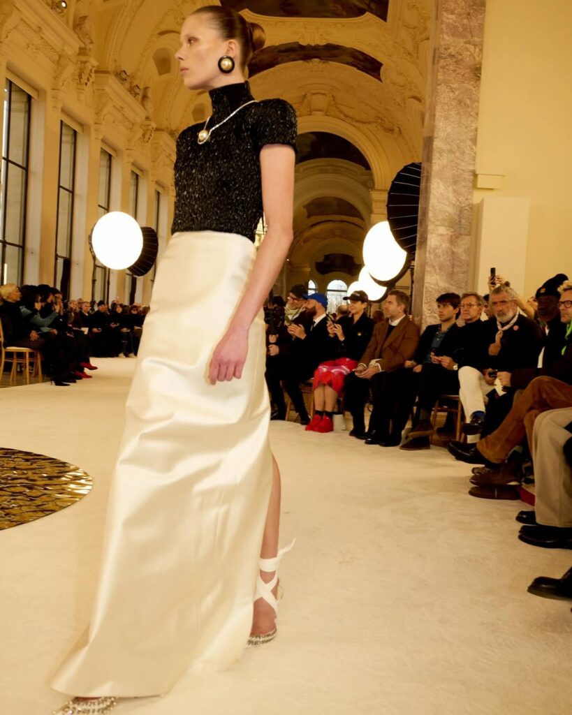 Schiaparelli Haute Couture Spring/Summer 2025, wearing a broad-shouldered black smocked vinyl top tucked into a double satin column skirt