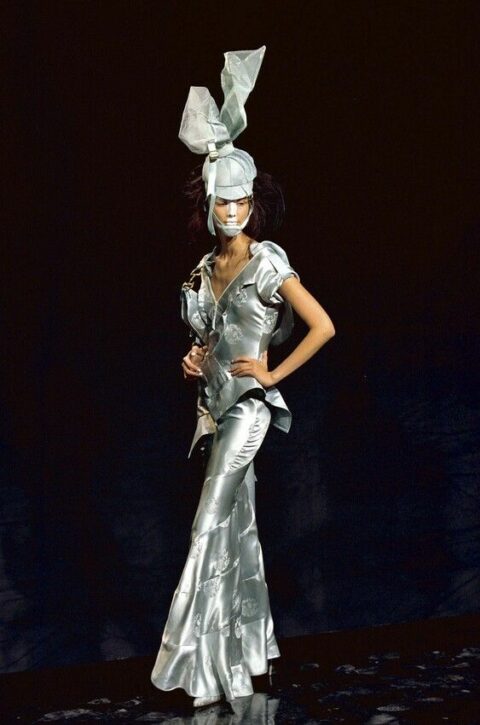 At John Galliano’s Christian Dior Spring/Summer 2000 fashion show, a model wears a satin dress with a matching sculptural headpiece.