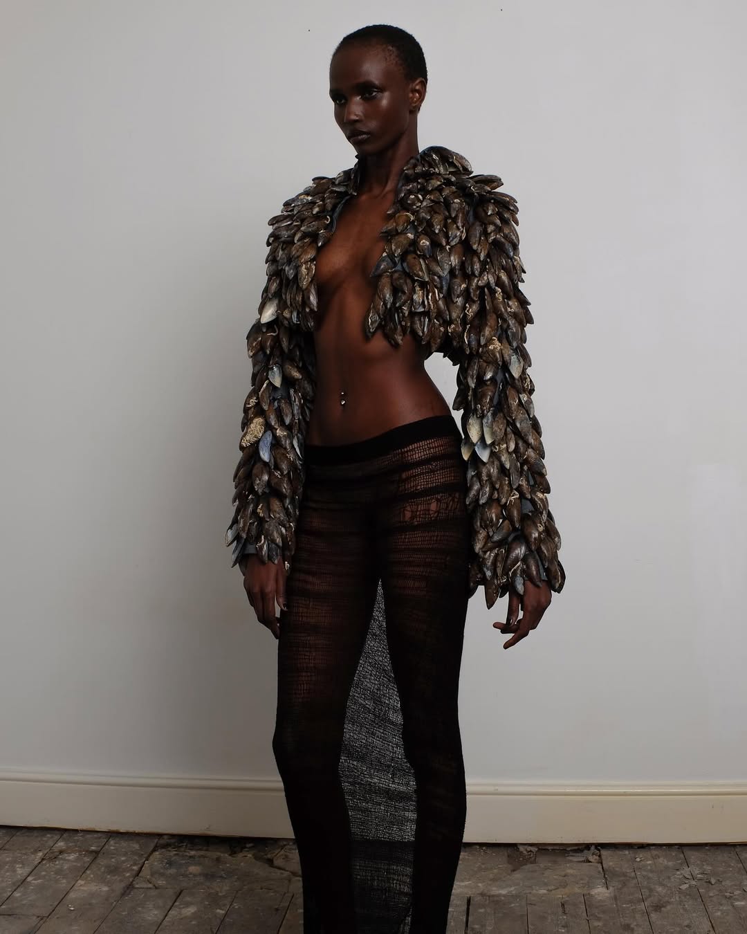 The George Trochopoulos Autumn/Winter 2025 collection titled “Défilé” included a shirtless look paired with a cropped bolero jacket made entirely of mussel shells and a low-rise sheer mesh knit maxi skirt.