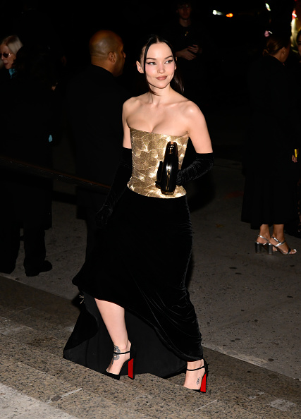 Dove Cameron arrives at the American Museum of Natural History for the 2025 CFDA Fashion Awards, wearing a Carolina Herrera metallic-embroidered bustier top, a velvet skirt with a train, velvet gloves, Christian Louboutin “Sandaloo” platform sandals, and a clutch.