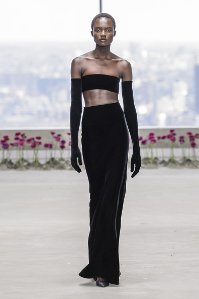 Ajus Samuel, a fashion model, showcases a black velvet three-piece bandeau crop top with long gloves and an evening skirt at the Carolina Herrera Fall/Winter 2025/2026 ready-to-wear collection fashion show.
