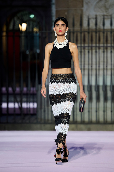 During the Carolina Herrera Spring/Summer 2026 collection show, a model graced the runway in a halter crop top, a striped, floral lace skirt, and a chic clutch in classic black and white.