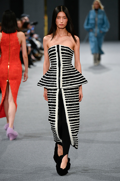 Model Xinyue Guo is pictured on the runway at the Balmain Womenswear Fall/Winter 2025/2026 show in an off-the-shoulder peplum gown with black and white horizontal stripes.