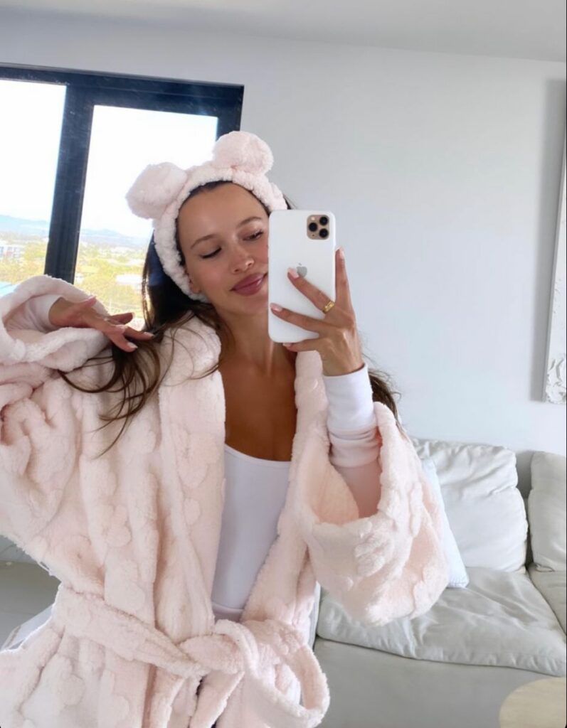 Model wearing fluffy ear hat holding phone in pink bathrobe