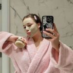 Model wearing mud mask in pink robe to display a daily skincare routine