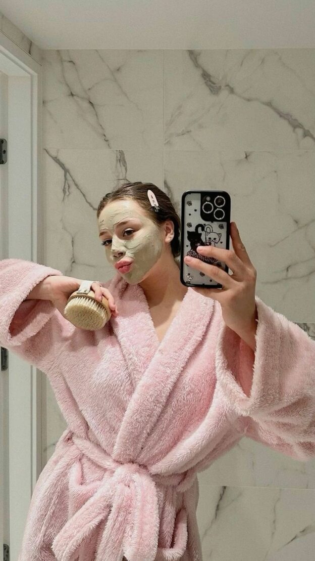 Model wearing mud mask in pink robe to display a daily skincare routine