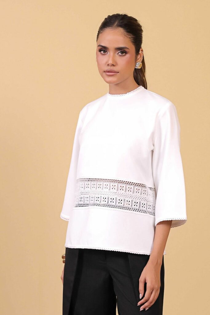 Model in white top with ornate stitching and black pants