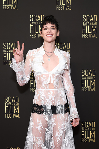 Kristen Stewart stuns at the 2025 SCAD Film Festival in a Rodarte lace costume including a bow-tie top and an asymmetrical midi skirt with black lace trim.