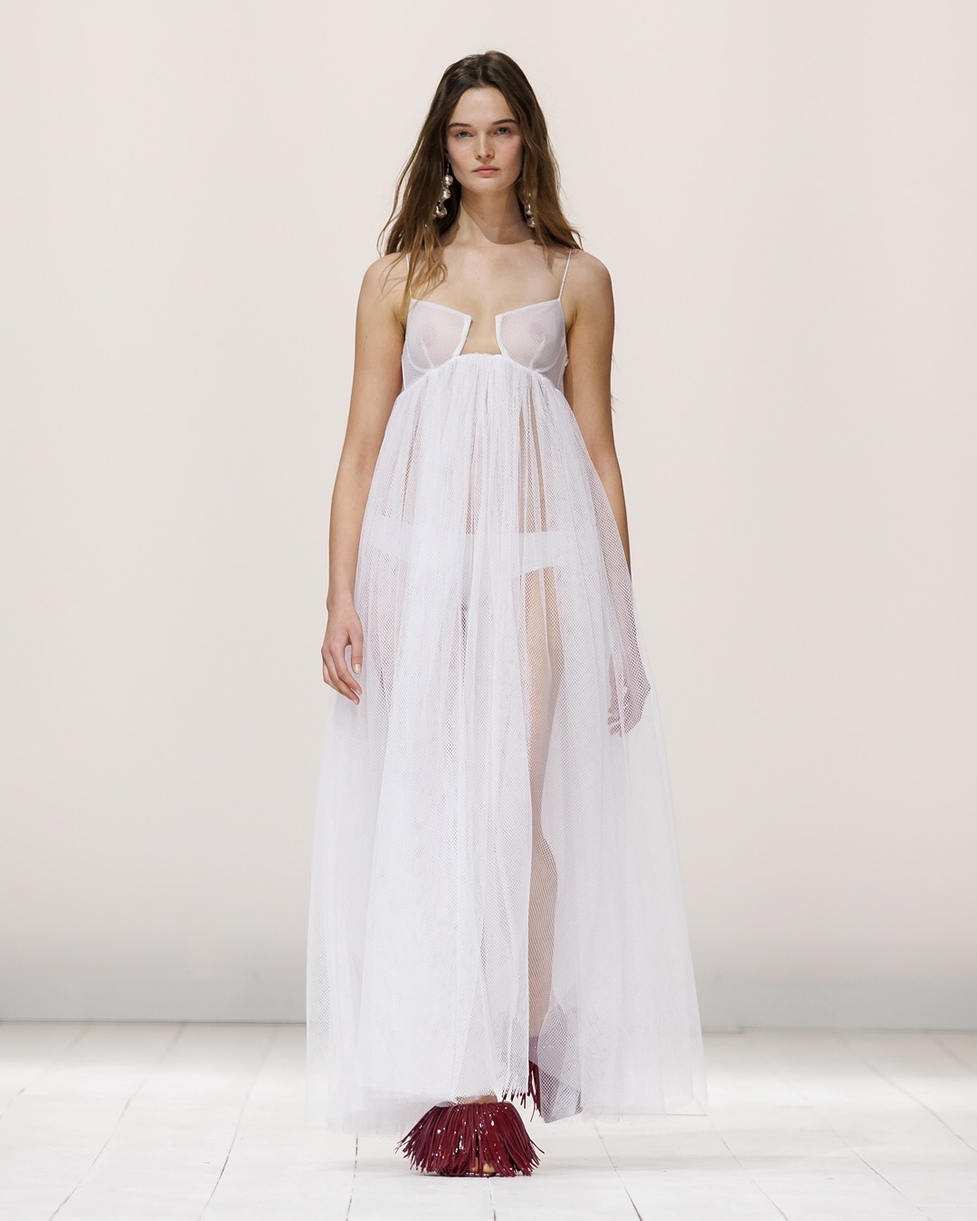 Lulu Tenney models a white cutaway diamond net maxi dress, spiky pearl earrings, and burgundy boudoir fringe mules for the Givenchy Spring/Summer 2026 ready-to-wear collection runway presentation