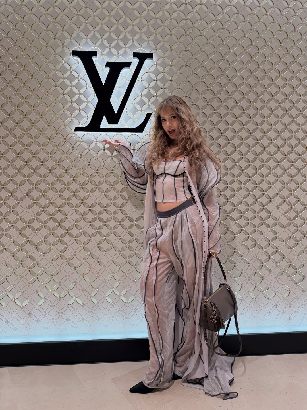 Lisa from BLACKPINK radiated elegance at the Louis Vuitton Visionary Journeys Seoul opening, donning a three-piece piping ensemble: a sheer duster jacket, a bustier-style crop top, and sheer, wide-leg pants.